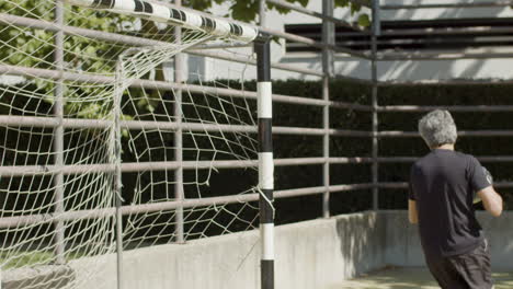 vista lateral de um goleiro sênior focado defendendo o gol de futebol e pegando a bola