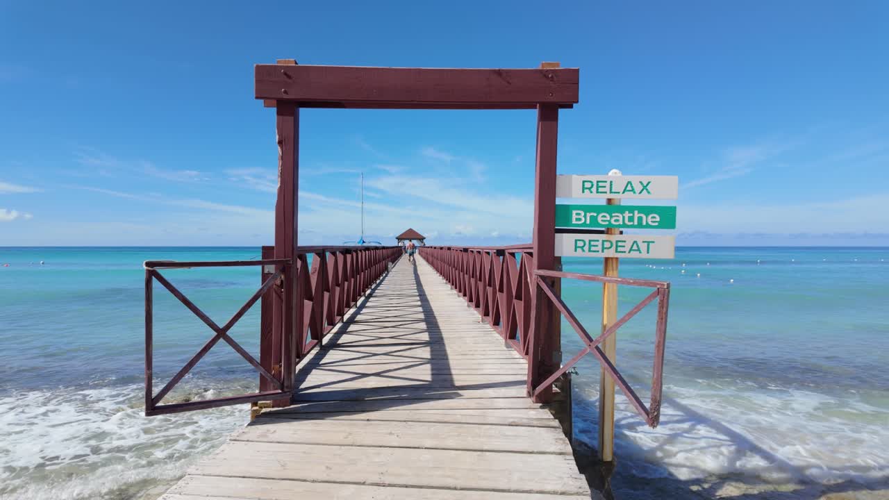 Static view of the entry signage on the wooden pier from the Dominican Beach, Dominican republic. Relax, Breathe, Repeat stress free message
