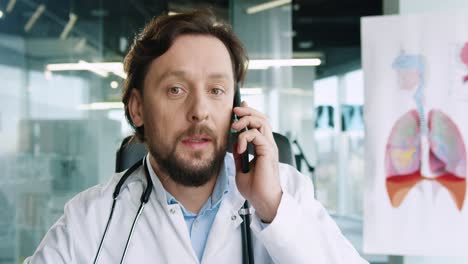 close-up view of caucasian senior male doctor with stethoscope sitting at desk and talking on the phone in hospital