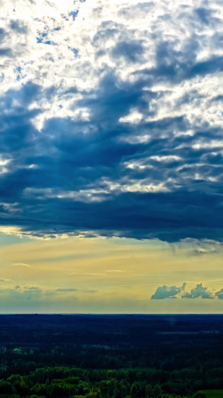 Dramatic clouds move over a forest landscape as sunlight breaks through at sunset