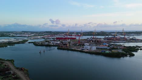 panorámica aérea de un puerto marítimo industrial con grúas de carga y muelles al atardecer
