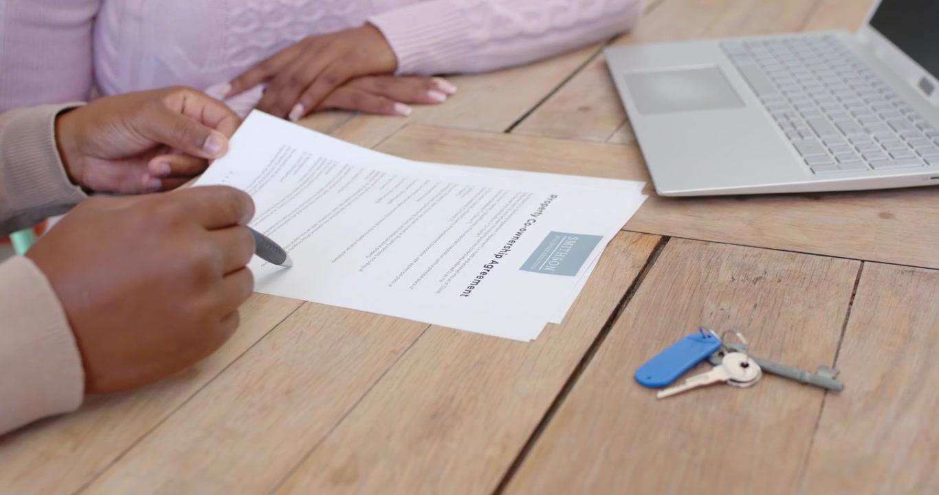 Consulente e cliente africani esaminano documenti stampati al tavolo, il consulente indica con la penna, il cliente osserva
