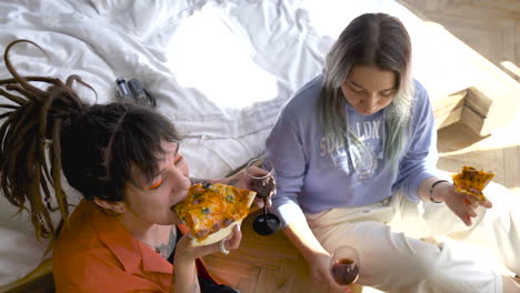 top view of two happy girls drinking wine and sharing pizza while laughing sitting on the floor at home 1