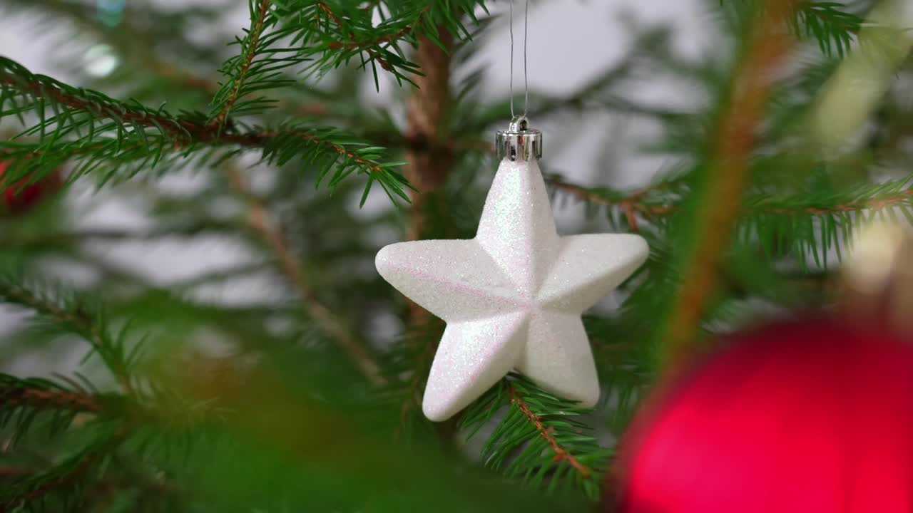 Close-up of a real Christmas tree branch with a white star ornament in focus and a red bauble softly blurred in the foreground, capturing a cozy festive holiday atmosphere