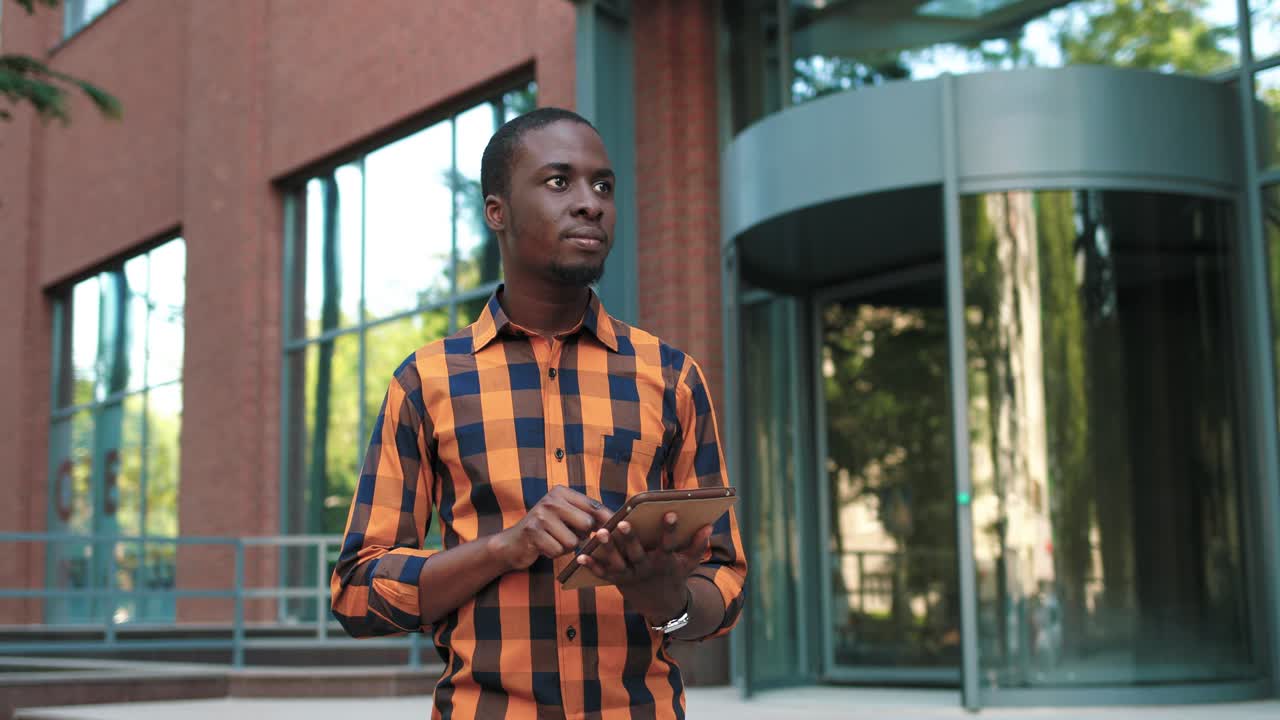 African american man using a tablet while preparing to exams during the break near the college