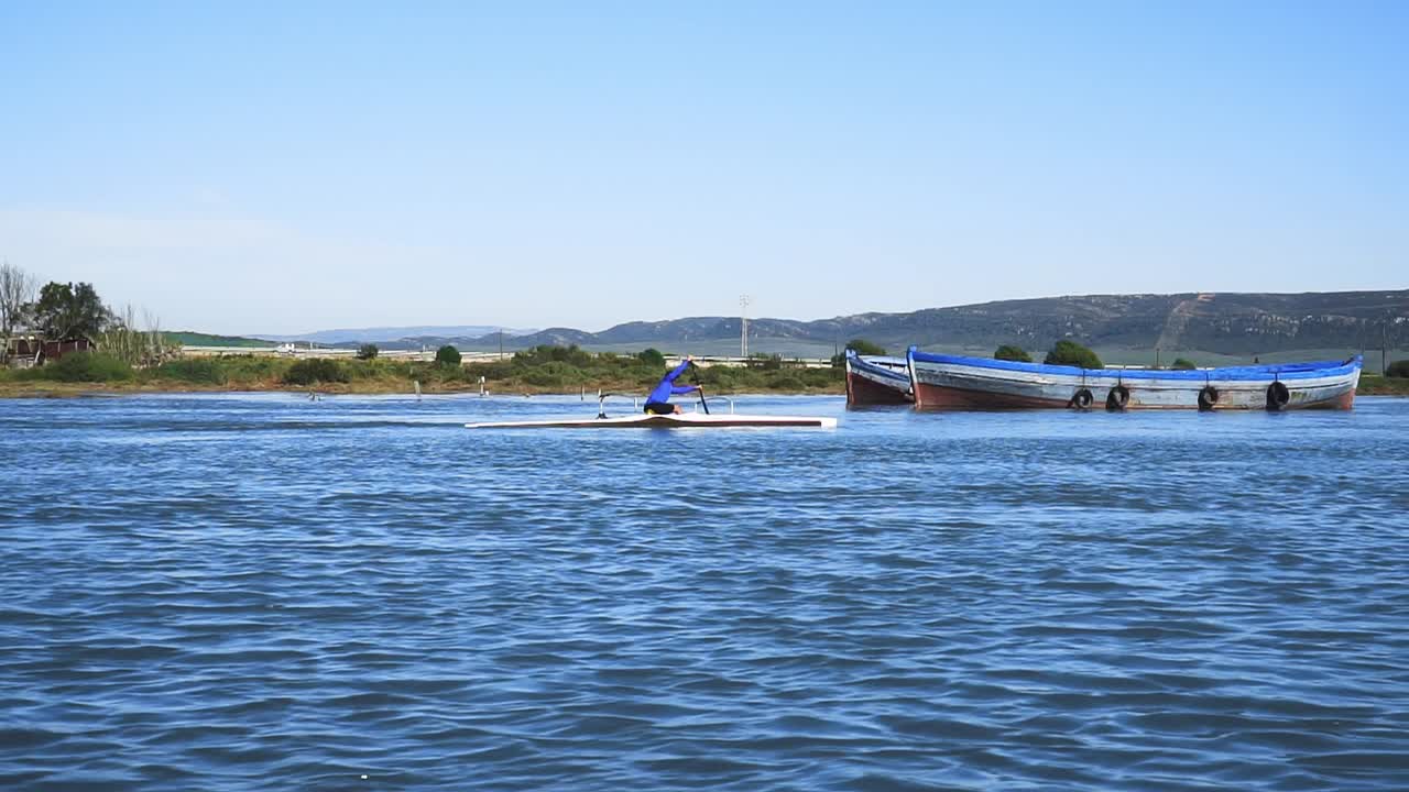 plano general de un hombre remando a cámara lenta en una canoa solitaria en un río a plena luz del día