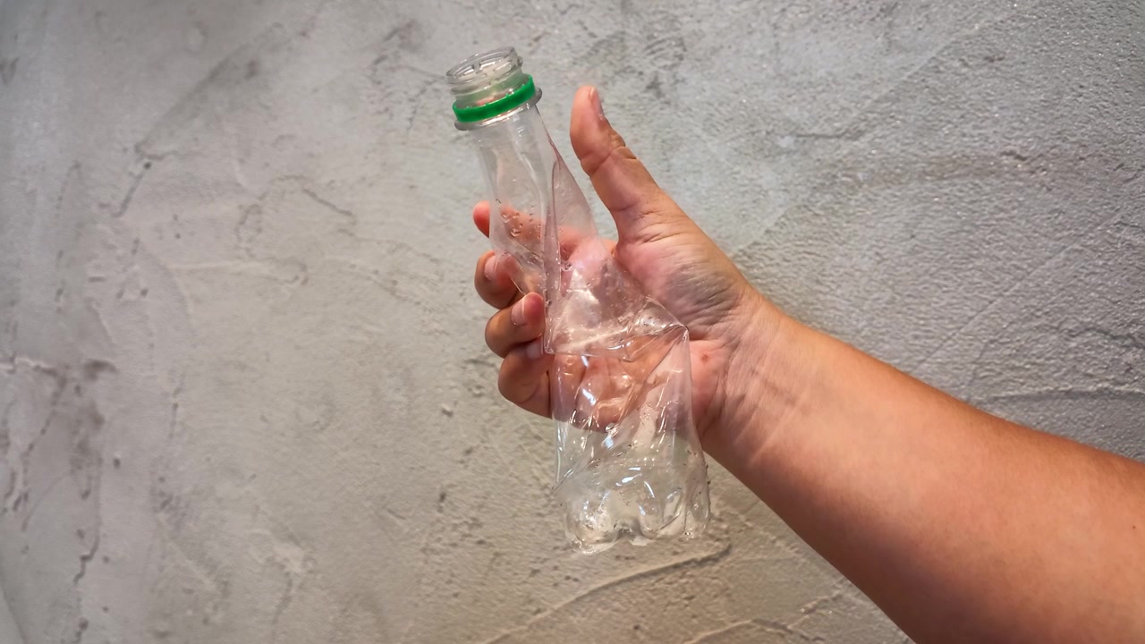 Primo piano di una mano che stringe una bottiglia di plastica trasparente per la riduzione dei rifiuti e il riciclo.