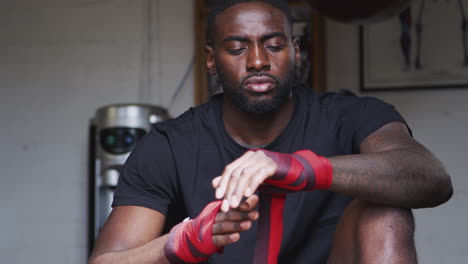 close up of male boxer training in gym putting wraps on hands standing next to punching bag