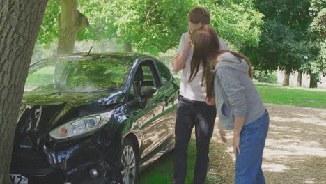 couple by smoking car inspecting accident damage and calling emergency services