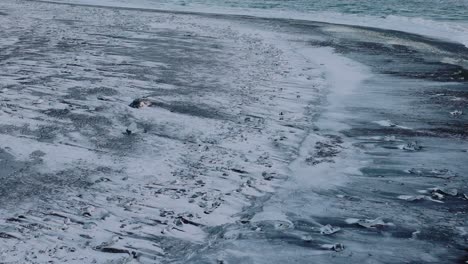 Luftaufnahme-über-Meereswellen,-Die-Bei-Sonnenuntergang-Auf-Den-Schneebedeckten-Diamond-Beach-Krachen