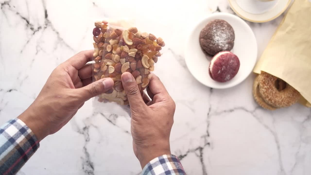 persona sosteniendo una bolsa de nueces mixtas y bocadillos en una mesa de mármol