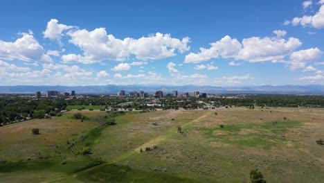 Fliegen-über-Die-Grüne-Wiese-Mit-Hochhäusern-In-Der-Ferne-In-Denver-City,-Colorado,-Usa