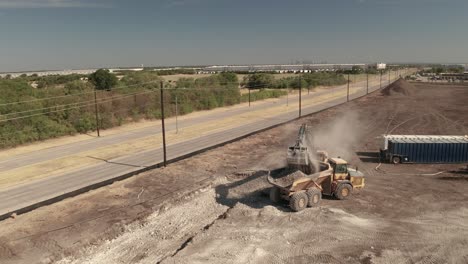 a dump truck gets filled with dirt and rocks by a crane loader