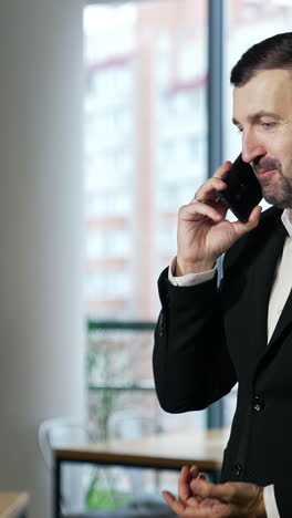 businessman having a pleasant conversation on the mobile phone. confident man has business talk on the phone. big windows at the backdrop. vertical video