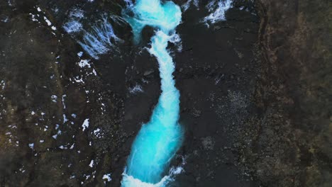 Aerial-tilt-up-shot-of-majestic-icelandic-waterfall-river-between-rocky-landscape-and-mountains-in-background