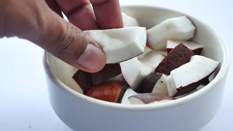 close-up of a hand picking pieces of fresh coconut from a white bowl