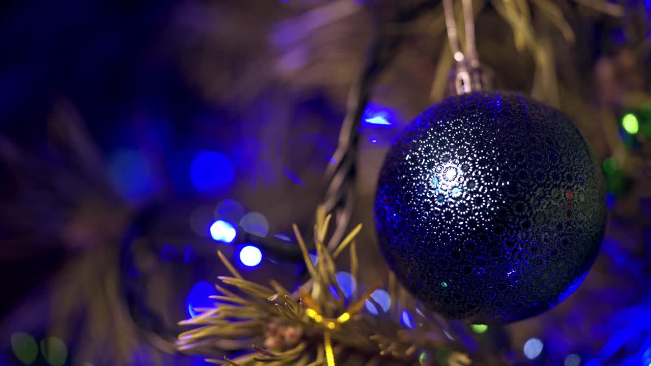 Beautiful Christmas ball hanging on a spruce tree. Christmas and New Year decoration on Christmas Tree with blue blinking background from garland.