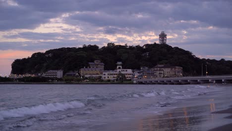 vista de ángulo bajo hacia la isla de enoshima en japón al atardecer con olas rompiendo en la playa