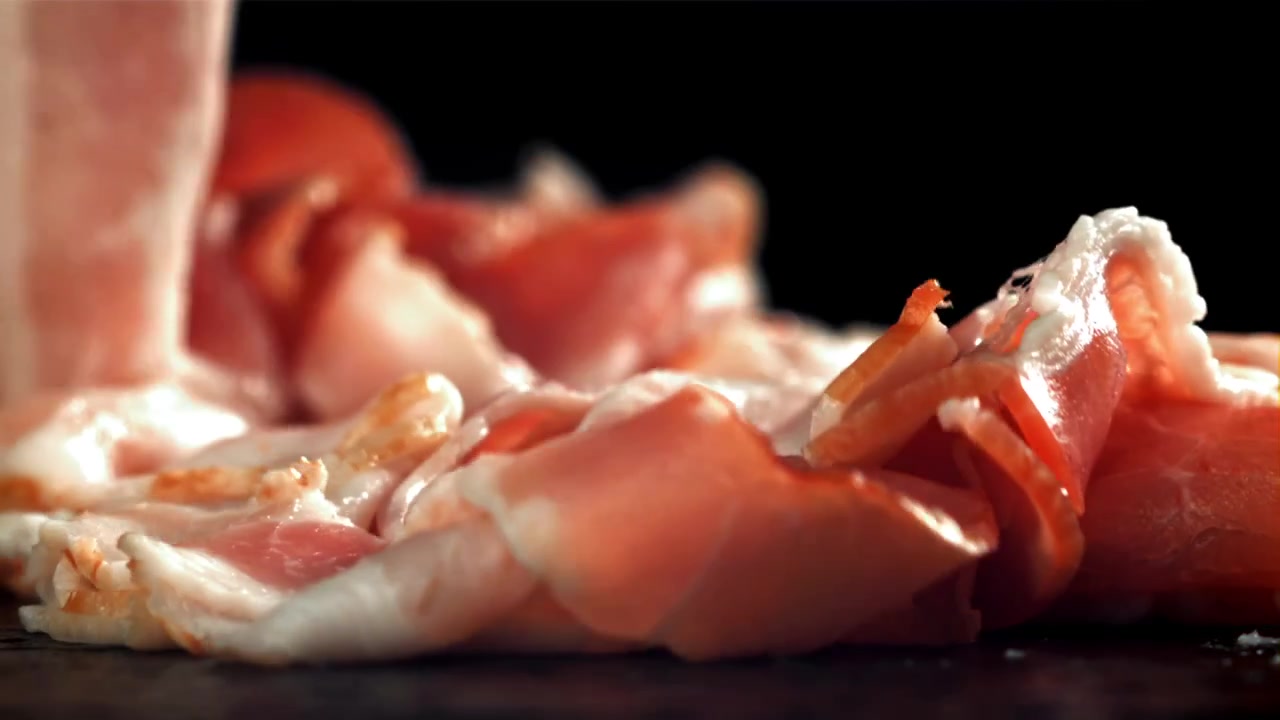 Fette di prosciutto che cadono al rallentatore su una superficie scura