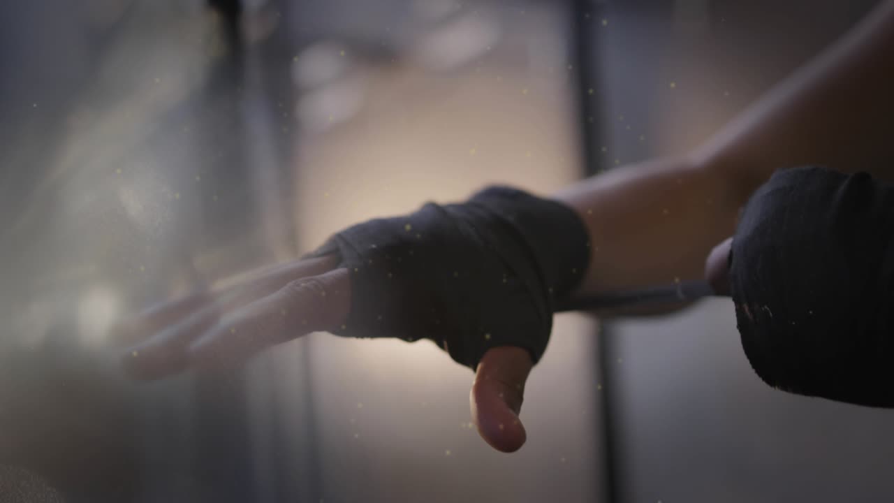 Mid-adult female athlete holding arm and tightening black wraps for training, camera pulling back