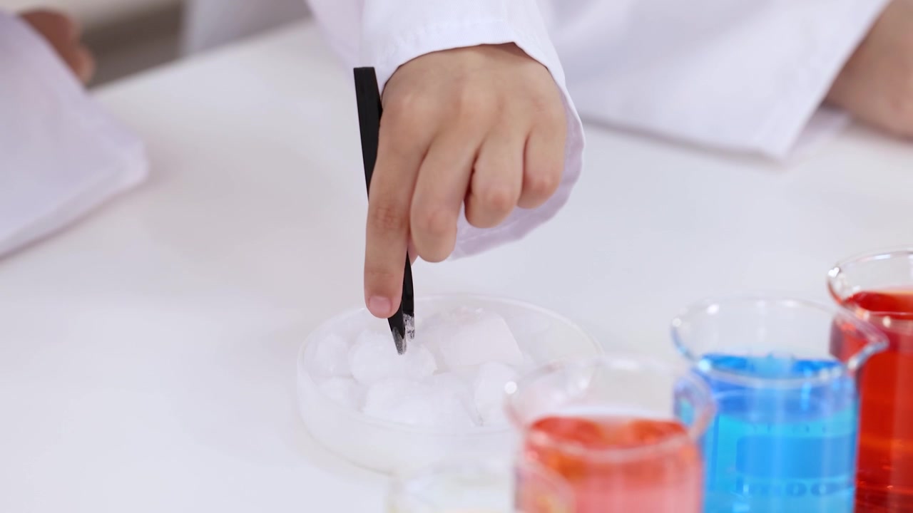 화학 수업 중 페트리 접시 안의 흰색 고체에 핀셋을 사용하는 아이 손의 클로즈업