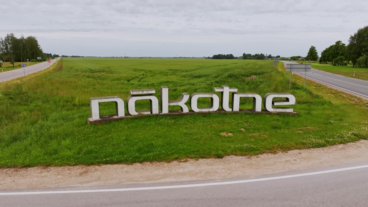 Aerial view of Nākotne town sign, Latvia under cloudy sky with surrounding field