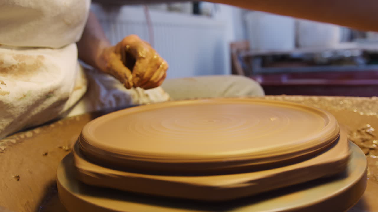 primer plano de un alfarero masculino moldeando arcilla para una placa en una rueda de cerámica en un estudio de cerámica
