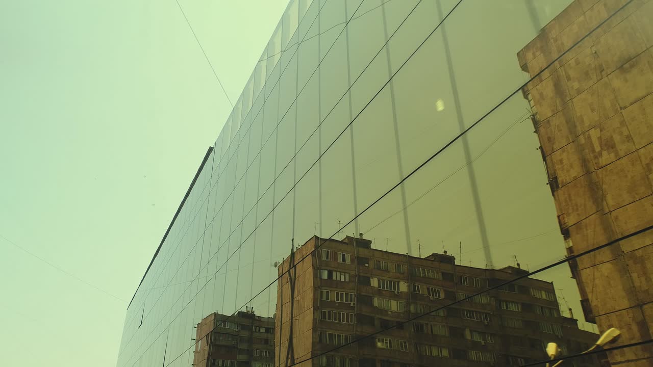 vista exterior de 4k de un edificio del distrito comercial o un centro comercial con ventanas de espejo de pared durante el día. luz solar. reflejo de la ciudad, coches y torres en paredes de espejo. cámara de avión no tripulado en movimiento