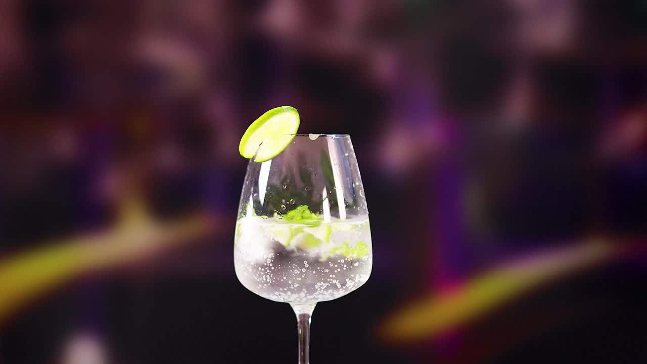 Un cocktail mojito con lime e menta in un vivace ambiente da bar, caratterizzato da illuminazione dinamica e un'atmosfera vibrante.