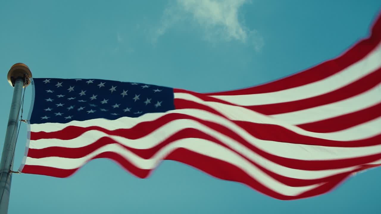 Close-up de bandeira americana tremulando ao vento contra um céu azul claro, símbolo patriótico da liberdade dos Estados Unidos.