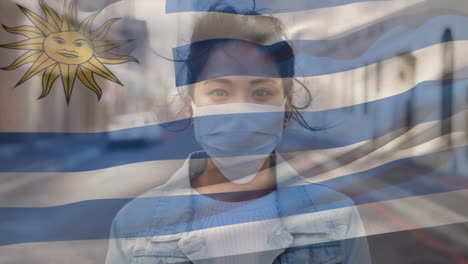 animation of flag of uruguay waving over woman wearing face mask during covid 19 pandemic