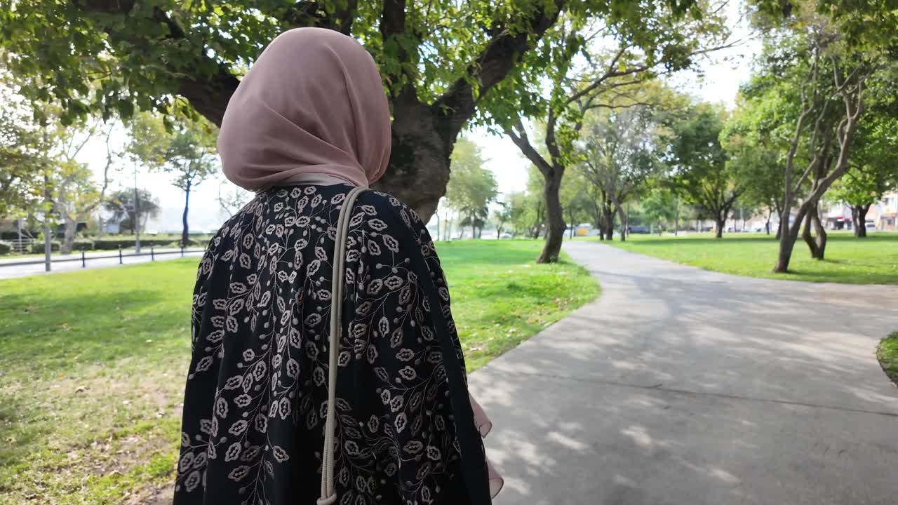 Back view of a woman in a hijab walking on a path in a park