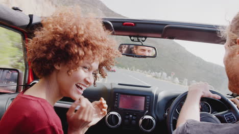 young couple driving open top hire car on summer vacation