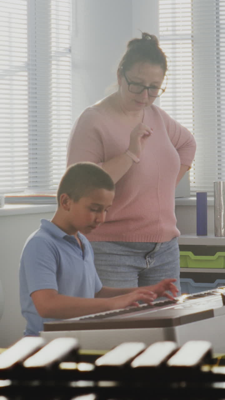 Music Teacher Guiding Primary School Boy to Play Piano in Music Class