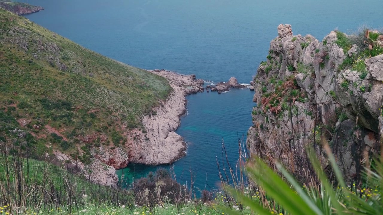 Una cala turchese appartata incorniciata da spettacolari scogliere calcaree e vegetazione costiera selvaggia sulla remota costa siciliana.