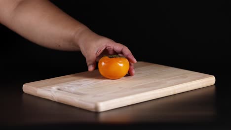 a hand reaches for a persimmon on a board