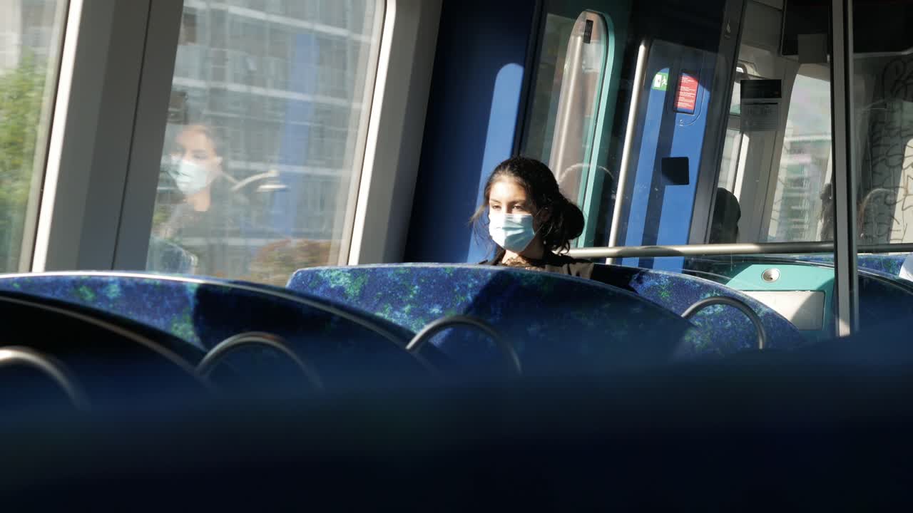 Young, sad looking woman in medical mask sitting alone in train