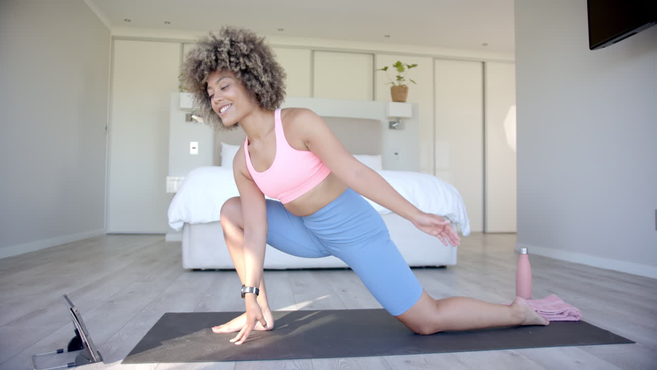 Smiling woman practicing yoga on mat in bedroom, stretching and exercising