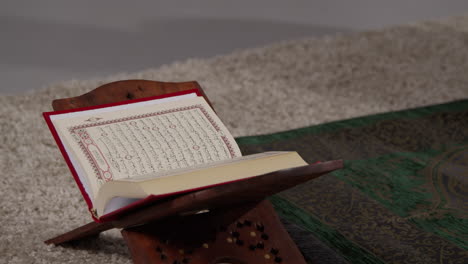 close up of open copy of the quran on stand next to prayer mat in muslim home 1