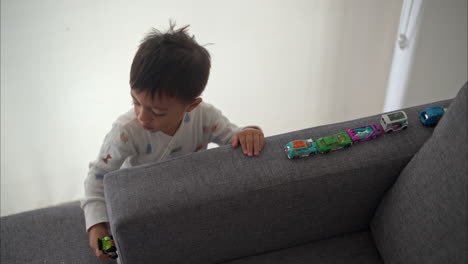 Tilt-down-shot-in-slow-motion-of-a-young-hispanic-boy-playing-with-his-car-toys-wearing-pajamas-on-a-cozy-morning