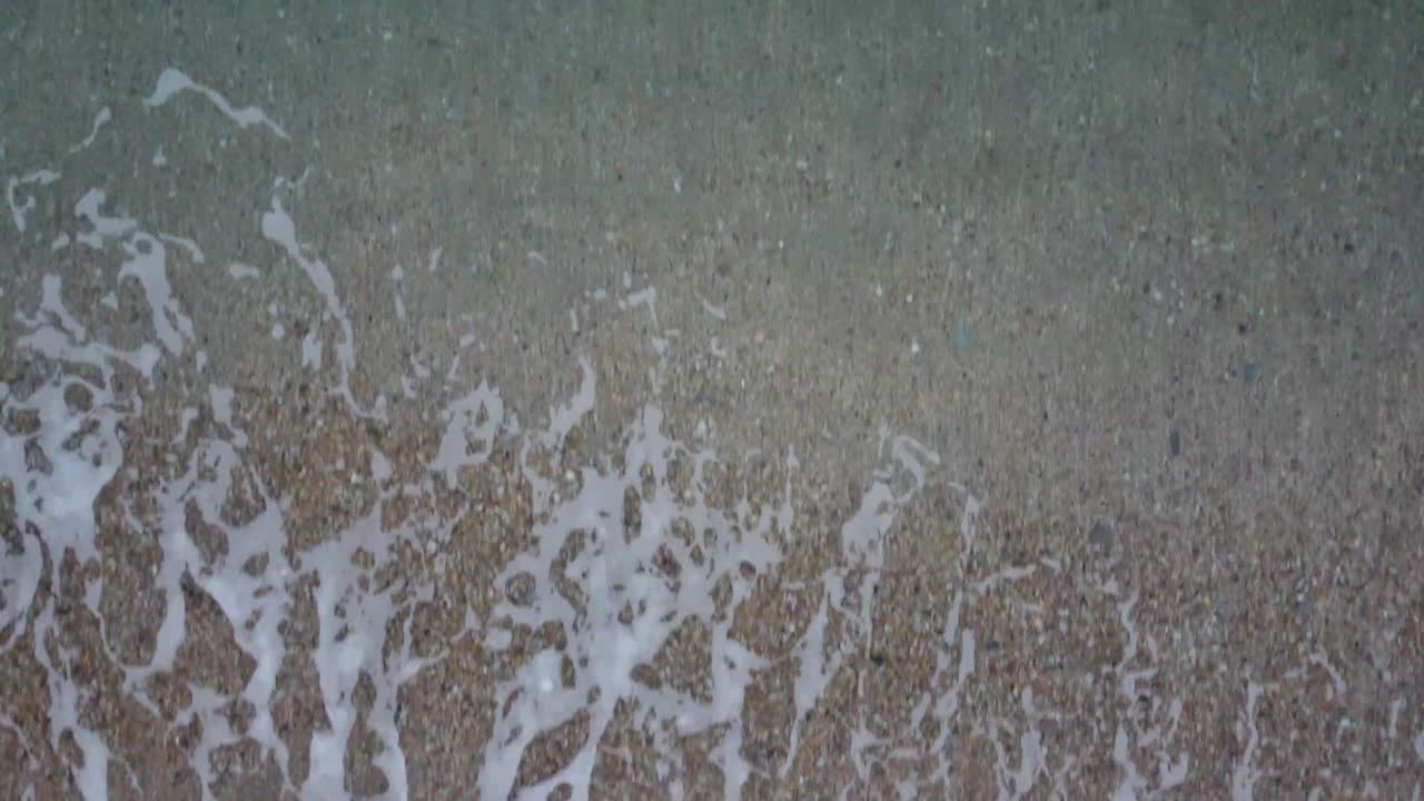 A Forwards moving drone shot starting top down above waves then slowly tilting up to reveal flat calm sea and a dusky sky