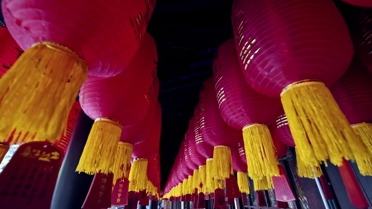 Lanternas vermelhas brilhantes com borlas amarelas formam uma exibição vibrante suspensa em um corredor de templo em Xangai. Ideal para documentários culturais ou reportagens de viagem.