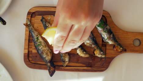 pouring lemon juice on grilled sardines