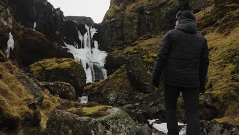 tourist stand in dark icelandic mountain environment with moss near waterfall