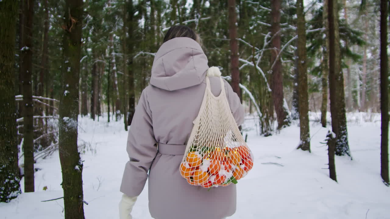 눈 인 숲 을 가로질러 그물 가방 에 오렌지 를 들고 있는 여자