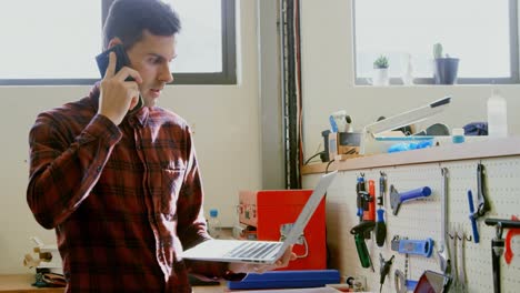 mecánico hablando por teléfono móvil mientras usa un portátil 4k