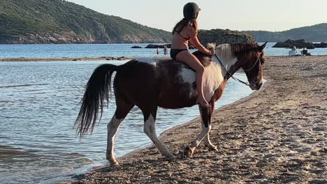 Young-red-haired-child-girl-in-bikini-have-fun-bathing-and-bareback-riding-horse-in-sea-water-in-summer-season