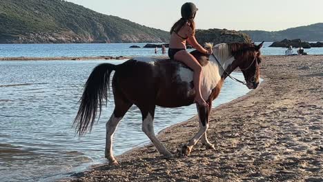 young red-haired child girl in bikini have fun bathing and bareback riding horse in sea water in summer season