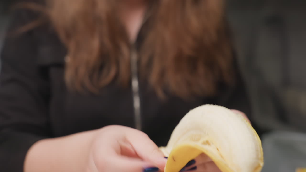 Close up female hands peeling banana from back then placing fruit on chopping board, blue manicure visible, kitchen background softly blurred, fresh snack preparation moment with gentle motion