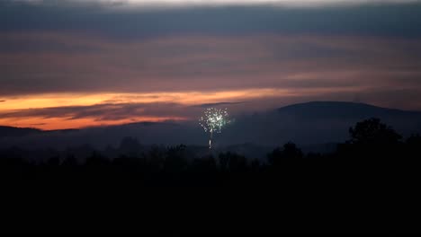 Shimmering-and-sparkling-light-from-exploding-fireworks-centered-against-dusk-sky-and-mountain-silhouette